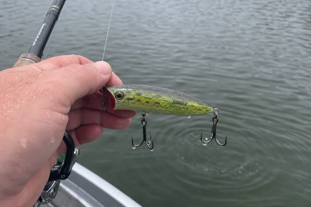 Våt hand håller i en grön Rapala Skitter Pop vid spöspetsen, ett av testets bästa abborre-beten 2026.