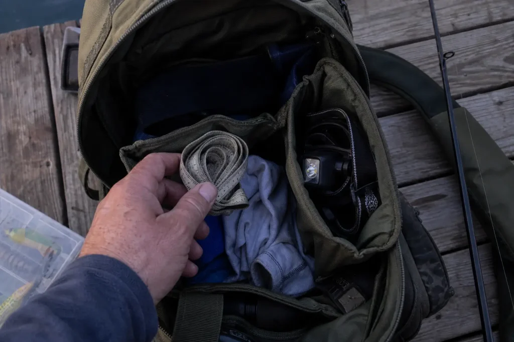 Packar fiskeutrustning i ryggsäck på brygga inför streetfisketävling Smålandsborren i skymningsljus