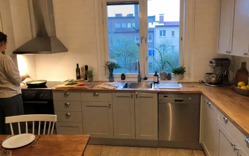 Kök med lax och dill på skärbräda medan kall sås till lax rörs ihop i en kastrull på spisen.