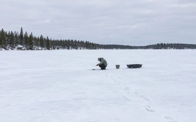 Person fiskar med mormyska spö vid ett hål i isen på en frusen sjö